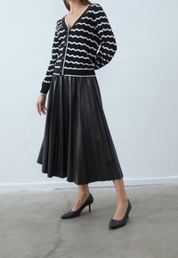 Svart och vit kardigan med vågmönster, i kombination med en plisserad svart imitationläderkjol och svarta spetsiga klackar.