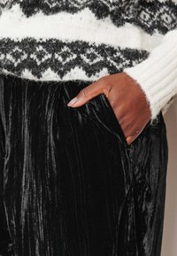 Pantalon en velours plissé noir à la texture douce, associé à un pull tricoté blanc avec un motif géométrique noir et blanc.