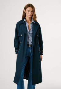 Manteau de marine avec grands revers, boutons double-breasted et poches latérales. Présente une doublure à carreaux et des poignets ceinturés. Assorti avec une chemise rayée.