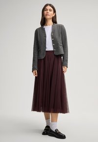 Cardigan grigio texturizzato con bottoni dorati, indossato su una camicia bianca e una gonna di tulle borgogna, abbinato a mocassini neri e calze grigie.