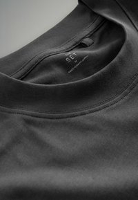 Schwarzes Baumwoll-T-Shirt mit rundem Ausschnitt und genähten Details. Pflegeetikett sichtbar im Kragen, Größe "M". Glatte Textur.