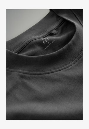 Čierne bavlnené tričko s okrúhlym výstrihom a šitými detailmi. Na vnútornom golieri je viditeľná etiketa s označením veľkosti "M." Hladká textura.