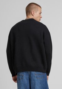 Svart strikket genser med en avslappet passform, med senkede skuldre og ribbestrikket kant. Kombinert med lyseblå, løse jeans.