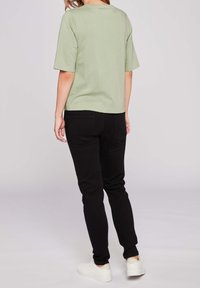 Zelený bavlněný top s krátkým rukávem kombinovaný s černými slim-fit kalhotami a bílými teniskami, prezentující jednoduchý, neformální design bez viditelných vzorů.