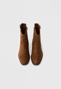 Καφέ σουέτ μποτάκια σουέτες με λείο φινίρισμα, διακοσμημένα με φερμουάρ στο πλάι, γλωσσάκι και ελαφρώς μυτερή μύτη. Πλατφόρμα με επίπεδο τακούνι.