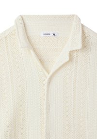 Camicia bianca a maniche corte in maglia con colletto, presenta intricati motivi testurizzati e cinque bottoni sul davanti; etichettata "Terranova XL."