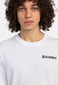 Hvid bomuld t-shirt med rund halsudskæring og korte ærmer, med et sort "ELEMENT" logo trykt på venstre bryst.