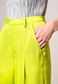 Jasnozielone spodnie wykonane z gładkiego materiału, z wysokim stanem, plisami i bocznymi kieszeniami. Wykończone pasem w tym samym kolorze.