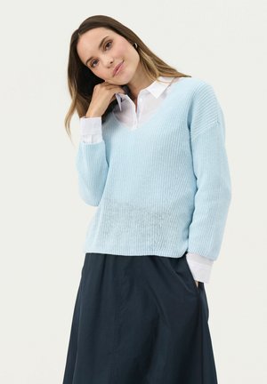 Light blue knitted sweater with a V-neck and three-quarter sleeves, paired with a white collared shirt underneath. Simple, textured design.