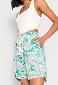 Vitt kort topp med gröna och blå blommönstrade shorts, med dragsko i midjan, duskdetaljer och spetsdetaljer vid fållen.