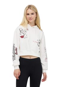 Felpa bianca accorciata con disegni e testo in nero e rosso, con cappuccio regolabile e maniche lunghe. Abbinata a leggings neri.