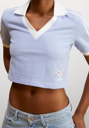 Jasnoniebieska krótka koszulka polo Adidas z białym kołnierzykiem, haftem kwiatowego logo, noszona z jasnymi dżinsami.
