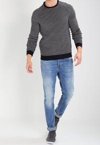 Pull tricoté bleu marine avec motif blanc, col rond et poignets côtelés. Associé à un jean bleu clair et des baskets grises.