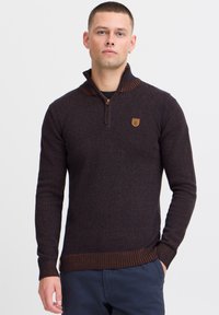 Ciemnogranatowy sweter z zamkiem przy kołnierzyku, z prążkowanymi mankietami i dolnym ściągaczem w kontrastującym brązowym kolorze. Teksturowany materiał z subtelnym wzorem.