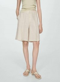 Beige linne shorts med en avslappnad passform, veckad front och sidfickor, kombinerade med neutrala sandaler. Slät textur och knälängd.