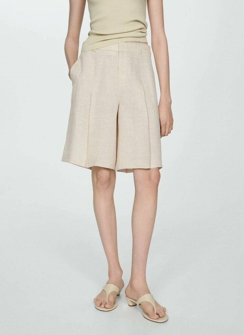 Beige linne shorts med en avslappnad passform, veckad front och sidfickor, kombinerade med neutrala sandaler. Slät textur och knälängd.