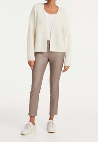 Gilet en tricot blanc à l'avant ouvert, associé à un pantalon ajusté bronze clair et des baskets blanches, mettant en valeur une texture douce et un design moderne.