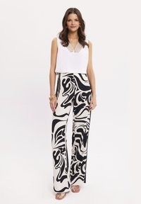 Biały bezrękawnik z dekoltem w kształcie litery V i koronkowymi detalami, w połączeniu z szerokimi spodniami w czarno-białe wzory z falującym motywem.