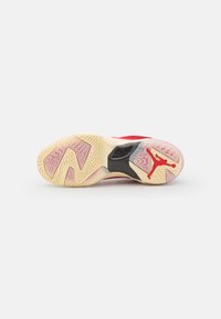 Semelle d'une chaussure de sport rouge et crème avec des grips texturés et un logo Jumpman rouge près du talon.