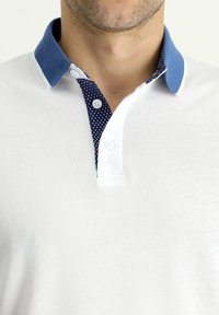 Camiseta polo blanca con un cuello azul y el interior del cuello de color marino con puntos; presenta cierres de botón, tejido texturizado y un corte clásico.