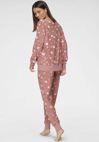 Pink loungewear set featuring a sweatshirt and pants. Both pieces have a soft texture and white heart patterns. Ribbed cuffs and waistband.