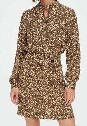 Braunes Kleid mit weißen, unregelmäßigen Flecken, langen Ärmeln, hohem Kragen mit Schlitz und einem gebundenen Taillengürtel.