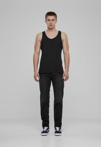Top negro sin mangas combinado con jeans oscuros y zapatillas negras. La camiseta tiene un escote redondeado. Los jeans presentan una sutil textura deslavada.