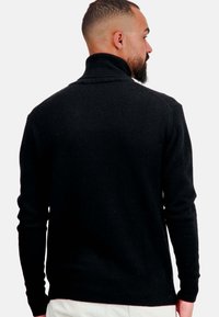 Pull noir avec un col montant, des poignets et un ourlet côtelés. Fabriqué en tissu tricoté avec une texture lisse, mettant en avant un design classique.