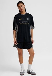 Sort sportstrøje med grå accenter og vertikale striber, med en fremtrædende logo og tekst. Kombination med matchende sorte shorts.