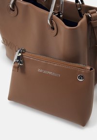 Brązowa torba typu tote ze skóry z srebrnymi okuciami, z tłoczonym logo oraz odpinaną dopasowaną saszetką na zamek z markowym detalem.