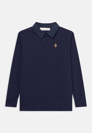 Polo a maniche lunghe blu navy con colletto scuro, patta con bottoni e piccolo logo giallo a forma di diamante sul lato sinistro del petto.