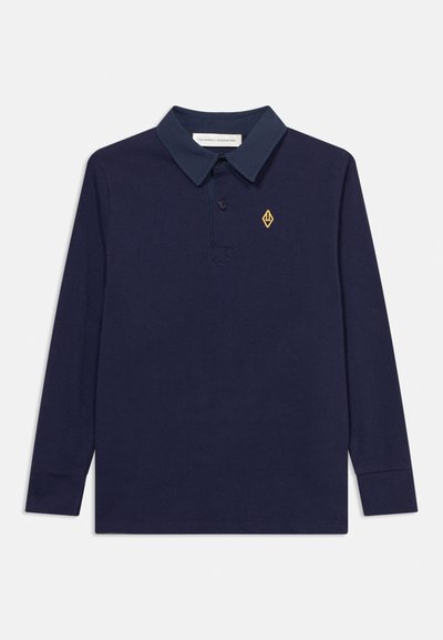 Polo à manches longues bleu marine avec col foncé, patte de boutonnage et petit logo jaune en forme de losange sur le côté gauche de la poitrine.
