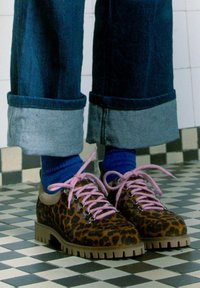 Scarpe maculate con lacci rosa e occhielli argentati, dotate di una suola spessa marrone. Indossate con jeans in denim arrotolati e calzini blu.