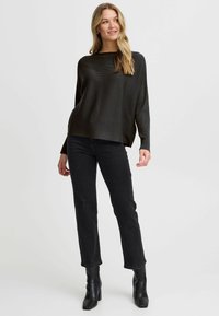 Zwarte ribgebreide trui met een ontspannen pasvorm, ronde hals en lange mouwen, gecombineerd met zwarte recht gesneden jeans en enkellaarsjes.