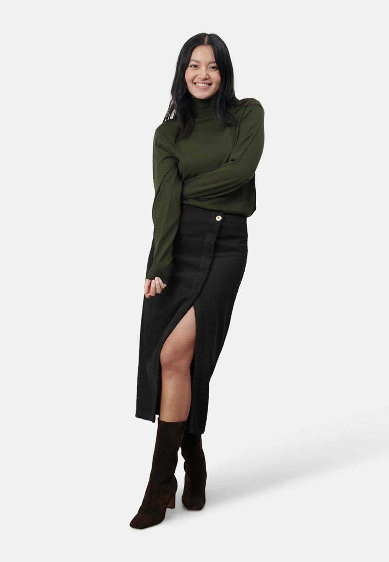 Olivgrüner Rollkragenpullover, schwarze gerippte Midirock mit seitlichem Schlitz und braune Wildleder-Stiefeletten mit Blockabsatz.