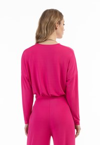 Maglia a maniche lunghe da donna in un vivace rosa, realizzata in un tessuto morbido. Presenta una vestibilità rilassata con spalle scese e un orlo arricciato.