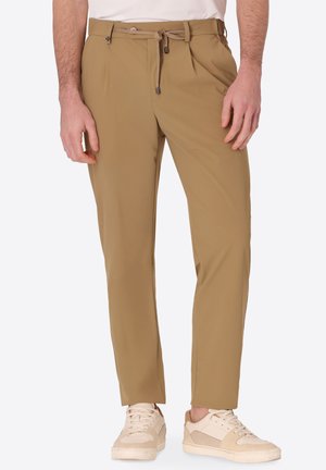 Uomo che indossa pantaloni beige a gamba dritta con vita annodata e sneakers casual beige e bianchi.