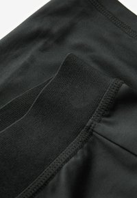 Svarta sportshorts med en slät yta, utrustade med ett brett elastiskt midjeband och plattlåsta sömmar för hållbarhet.