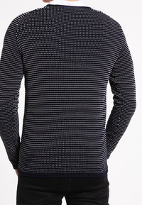 Pull en maille bleu marine à pois blancs, manches longues et encolure ronde. Tissu texturé avec une coupe ajustée et un ourlet côtelé.