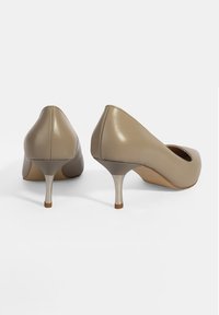Chaussures à talons hauts en cuir beige avec un bout pointu et un talon métallique argenté. Texture lisse avec des détails de couture minimaux.