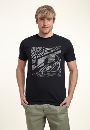 Schwarzes Baumwoll-T-Shirt mit einem grauen Grafikdesign, das den Text "JT Racing", kreisförmige Muster und Reifenprofil-Details auf der Vorderseite zeigt.