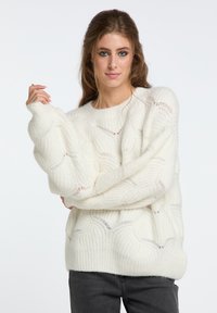 Maglione bianco con motivo a pizzo, realizzato in morbido tessuto a maglia testurizzato, con maniche corte e collo rotondo, abbinato a jeans scuri.