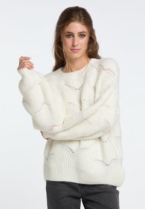 Pull cu model de dantelă, alb, confecționat dintr-un material tricotat moale și texturat, cu mâneci largi și guler rotund, asortat cu blugi negri.