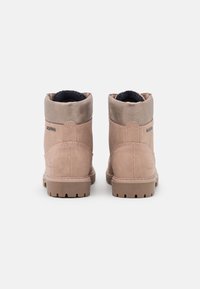 Bottes ankle en daim marron avec une doublure en polaire douce, dotées d'un bout arrondi et d'une semelle en caoutchouc texturée. Accent arrière avec le logo de la marque.