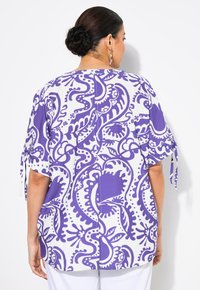 Top floreale a righe viola e bianche con maniche corte e dettagli a nodo. Realizzato in tessuto leggero con una vestibilità ampia e rilassata.