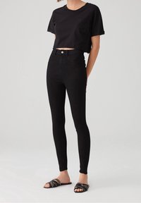 T-shirt nera cropped con maniche corte e tasca, abbinato a jeans skinny neri a vita alta e sandali neri con dettagli a borchie.