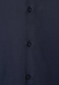 Close-up of dark blue fabric with three black buttons sewn in a vertical line.