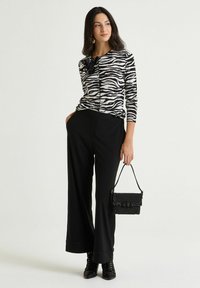 Maglione a maglia con stampa zebrata in bianco e nero e maniche lunghe, abbinato a pantaloni neri a gamba larga. Accessoriato con una piccola borsa a tracolla nera con paillettes.