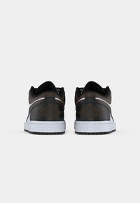 Pár čiernych, hnedých a bielych nízkych tenisiek Air Jordan zobrazených zozadu na neutrálnom pozadí.
