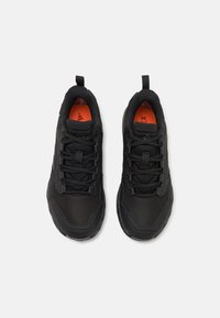 Black athletic shoes with a textured upper and mesh sections. Features include laces, two pull tabs, and an orange insole detail.
